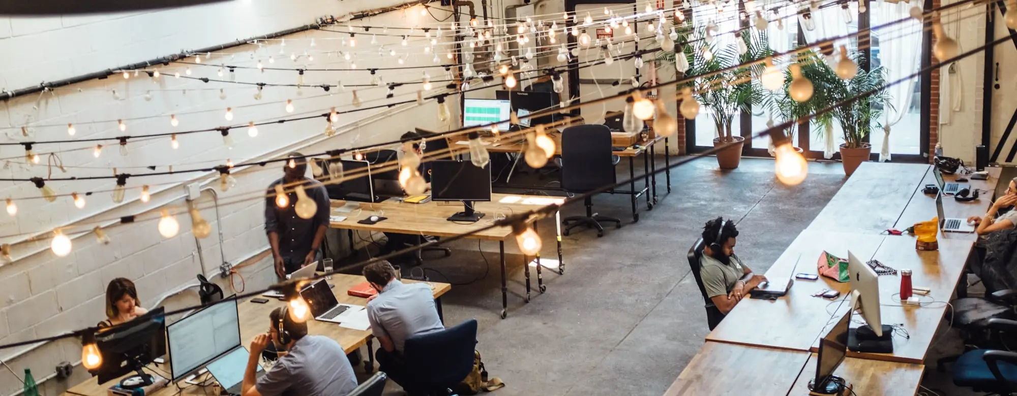 Widok z góry na przestrzeń coworkingową: długie stoły, rośliny i girlandy pod sufitem